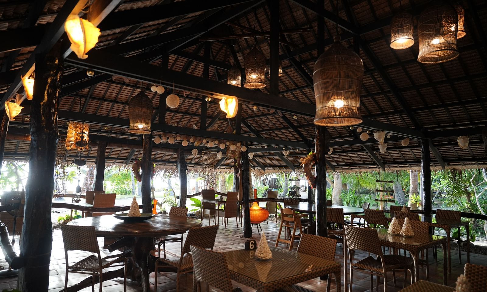 Restaurant seating at Flower Island Resort with white chairs and wooden tables under a thatched roof with ceiling lights.