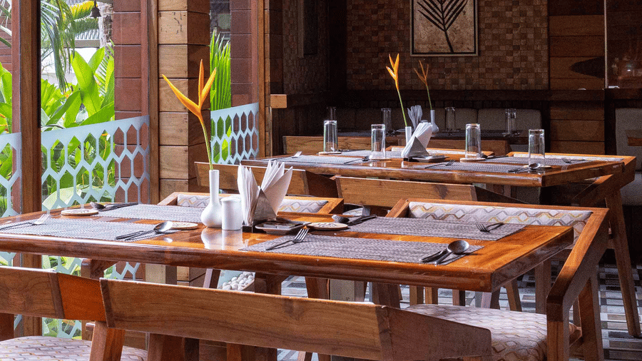 A restaurant with wooden furniture, with a balcony view to the lush greenery outside.