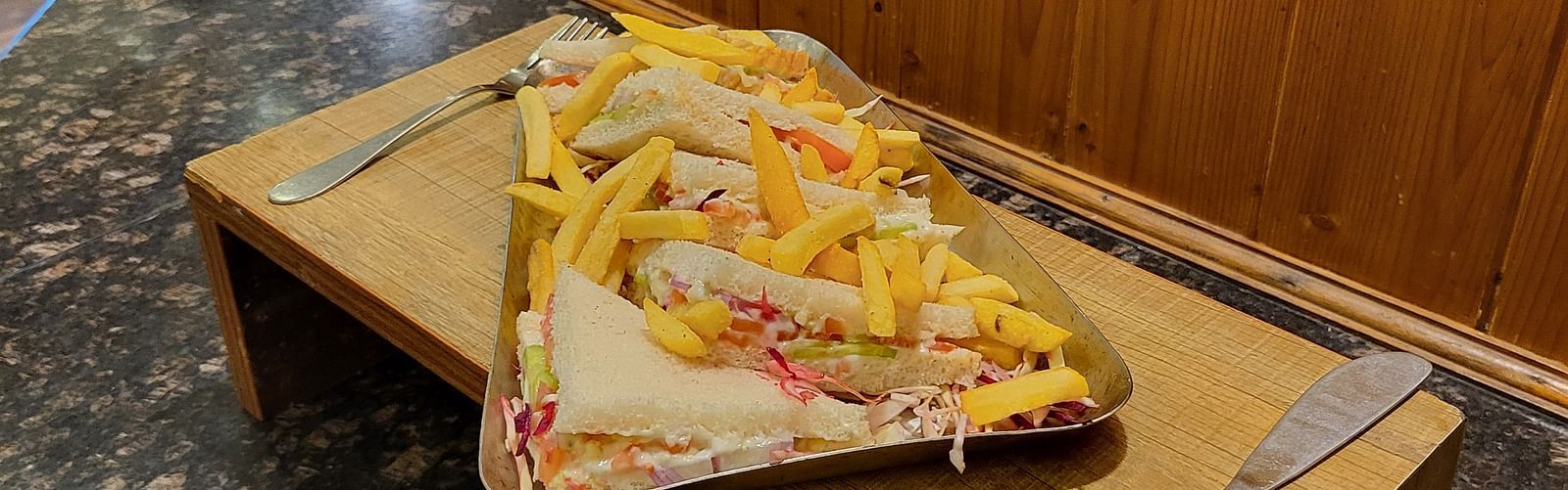 Sandwich on a wooden tray with a knife on the side at Dagshai Manor Kasauli - Inde Hotels.