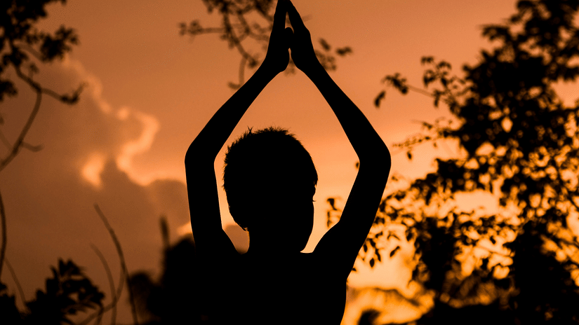 A silhouette of an individual with their hands raised is captured against an orange, sunlit sky.