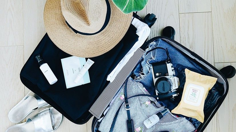 An open suitcase with things inside and a cap and other things kept next to it