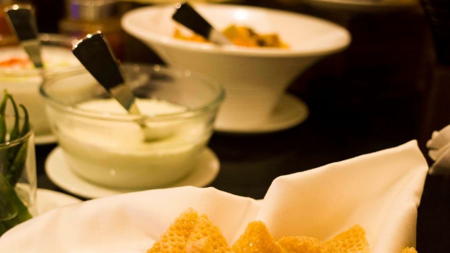 A basket of crispy, triangular fried snacks next to a white bowl of dipping sauce | Daksh The Madhuvan Suites