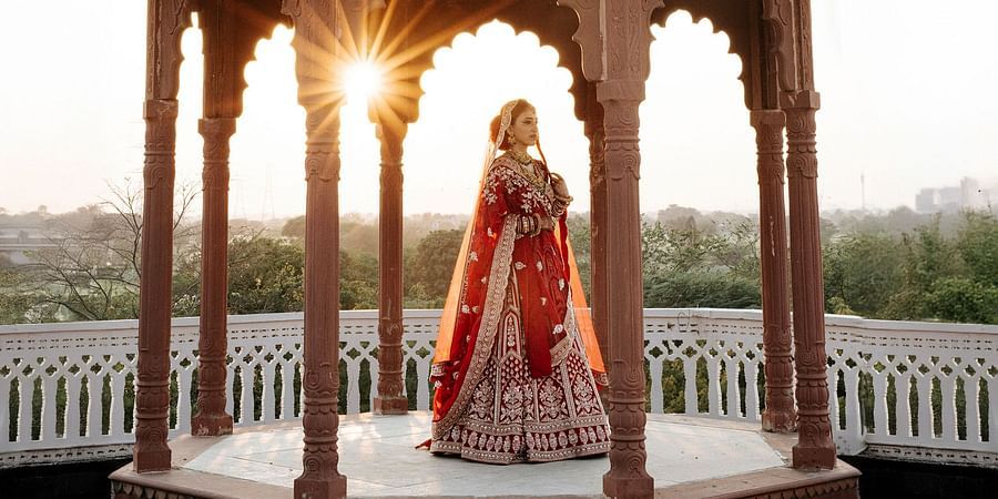 Bride standing in traditional attire inside red sandstone dome at sunset.