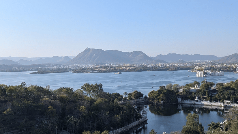 Captivating aerial view of Udaipur's serene lake and lush greenery under clear skies.
