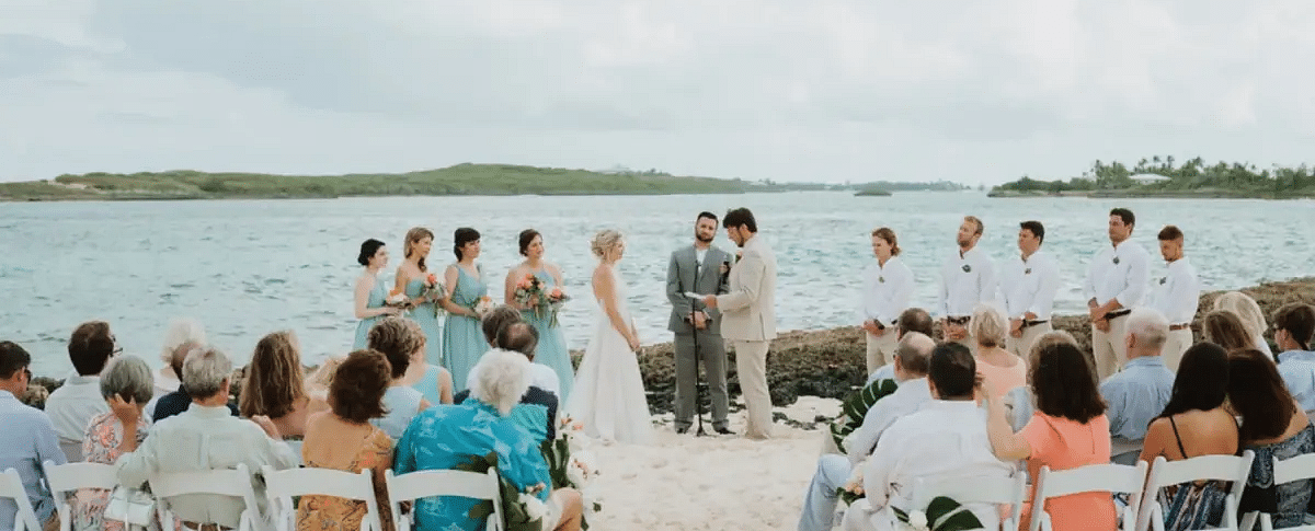 Beach wedding ceremony with guests seated on white chairs, facing the couple under an open sky with the sea behind | Abaco Inn