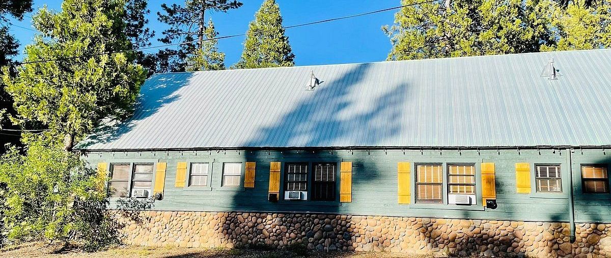 Exterior of Shaver Lake Village Hotel surrounded by trees on a clear, blue day.