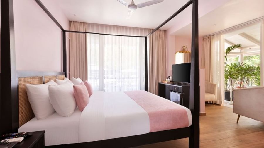 A daytime view of a room featuring a neatly made, beautifully decorated bed, a TV, a storage cabinet, and a balcony with comfortable seating arrangements.