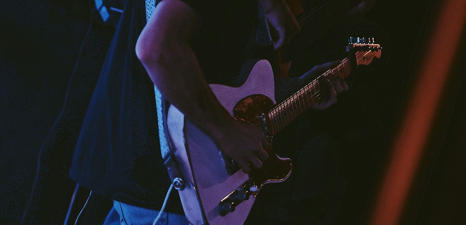 Musician playing guitar under stage lights during a live performance.