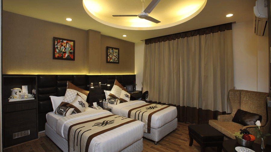 A Superior Twin Bed Room at JRD Exotica - Business Hotel featuring twin beds, an armchair with an ottoman, and modern lighting.