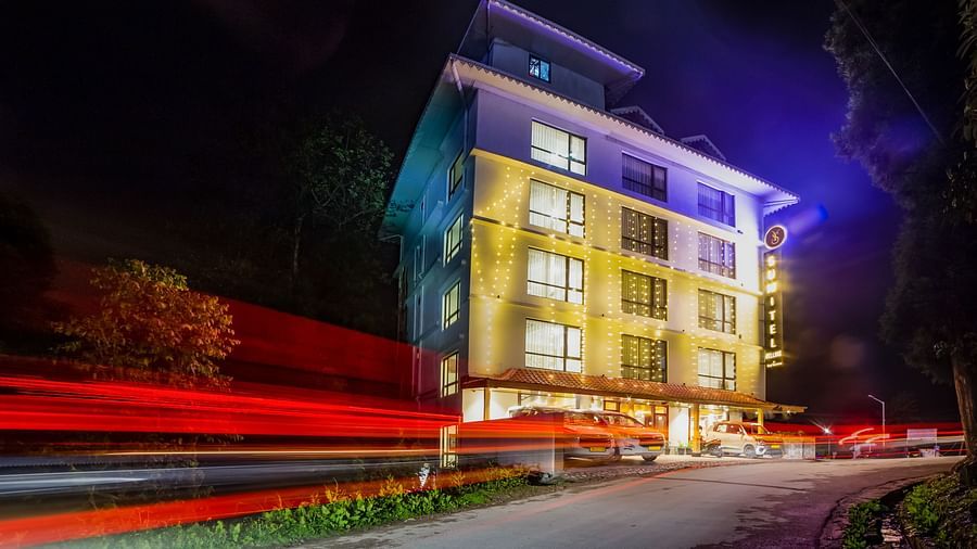 Nighttime view of the Sumitel hotel building, lit up with colourful lights, long exposure effect showing red car lights.