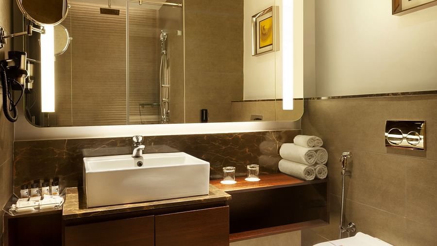 A spacious washroom with a large wall-mounted mirror, a washbasin below it, and a western toilet to the side | Cenneys Gateway