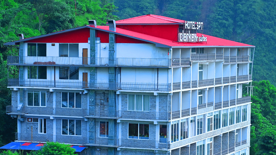 Facade of SPT Clarks Inn Suites, Mandi amidst lush greenery with a glimpse of a mountain in the bakcground