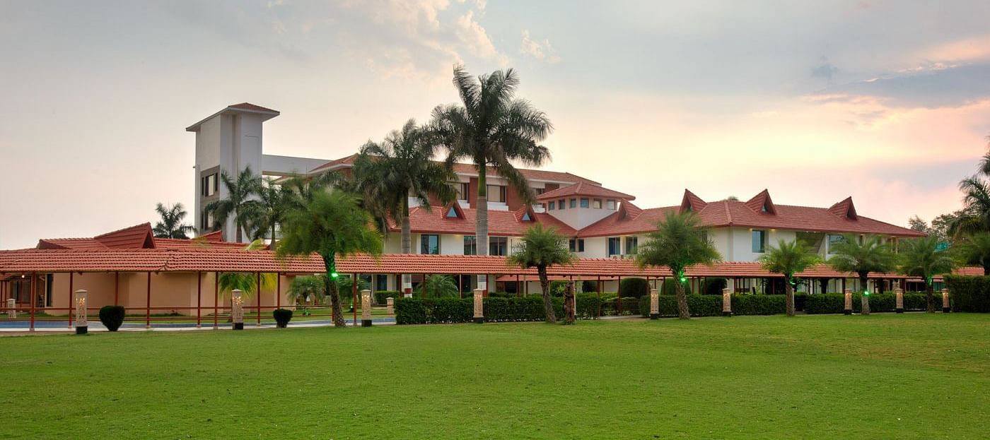 Exterior view showcasing lush grass and palm trees encircling the resort under a partly cloudy sky  | Crescent Spa & Resorts