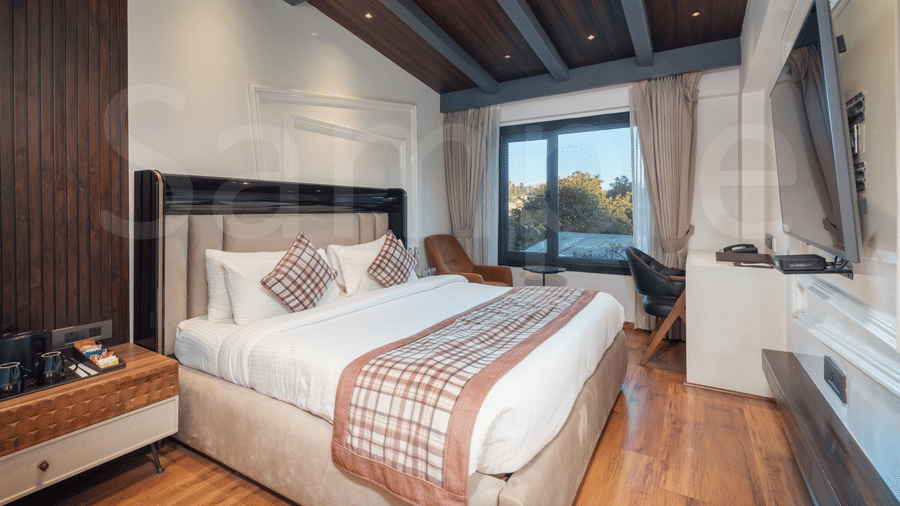 A bedroom with a bed, a wooden ceiling with dark beams, and a large window overlooking a hilly landscape | Lawrence Solitaire Resort, Nainital