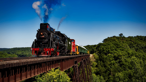 A locomotive train running amidst lush green landscapes.