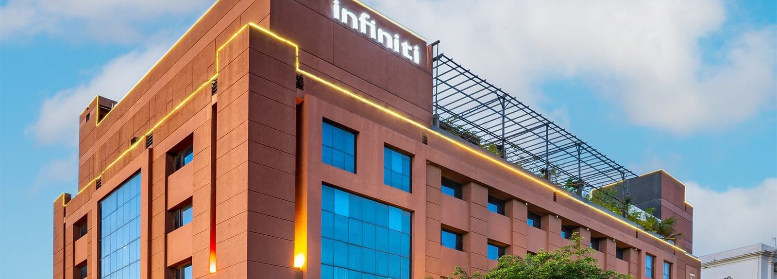 Exterior view of a multi-storey Infiniti Hotel, Indore with large glass windows, landscaped greenery, and visible signage on the top.
