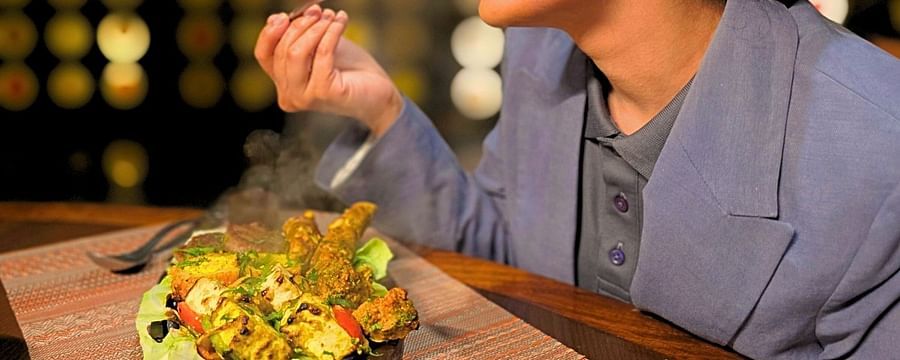 A close side angle of a woman dressed professionally, enjoying BBQ at a restaurant, with a plate of grilled food in front of her.