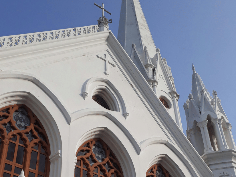 Low-angle view of white pointed arches and spires of a church building against a clear blue sky.