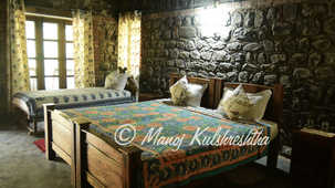 A rustic bedroom interior featuring two wooden beds against a exposed stone accent wall.