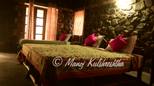 A warmly lit rustic bedroom with stone walls, wooden beds, and bright pink accent pillows.