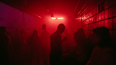 An overview of a night club with red light and silhouettes of people in view