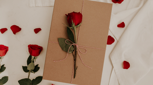 an envelope sealed with a rose on a bed with rose petals and flowers