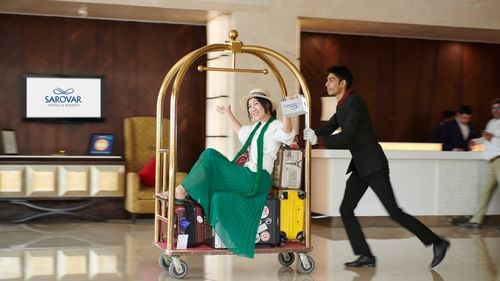 A woman being carried by a bellhop on a luggage cart - Grand Continent, Brookefield - A Sarovar Portico Affiliate Hotel
