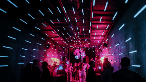 An overview of the entrance to a club with LED strips on the roof and people waiting