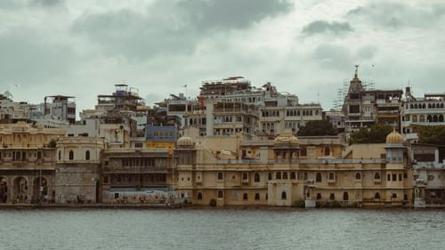 A view from lake pichola of the old run down buildings on the other side with dark clouds above
