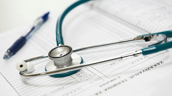 A stethoscope and a blue pen rest on top of printed paper documents on a light surface.
