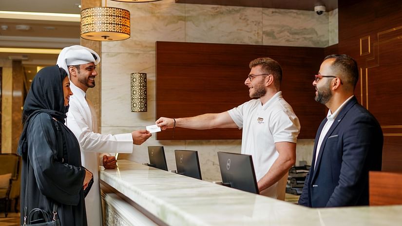 people behind the reception desk giving a keycard to the guests - La Maison Hotel, Doha