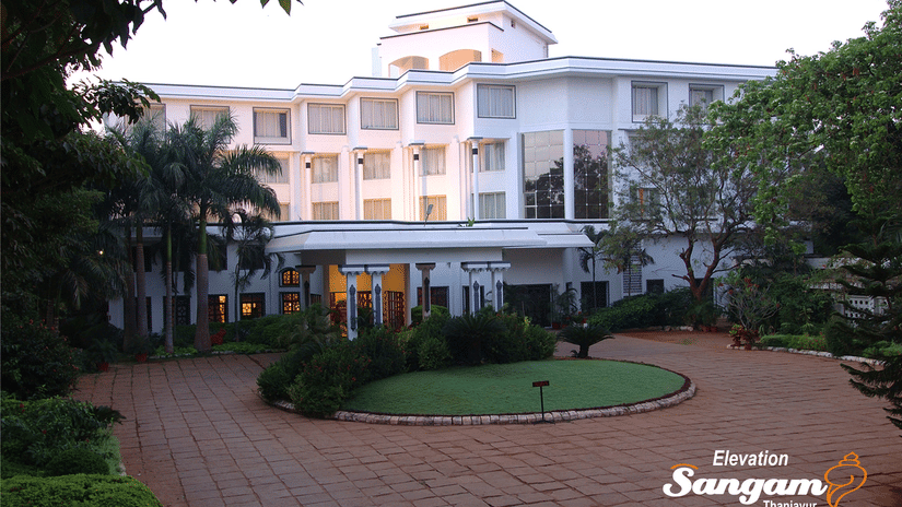 Facade view of Sangam Hotel, Thanjavur, with a pathway, a manicured garden and trees in view - Thanjavur Hotel Contact