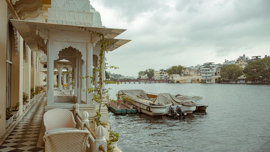 View from a balcony overlooking Lake Pichola in Udaipur, India, with boats docked and a bridge in the distance.
