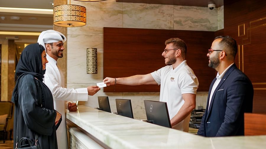 people behind the reception desk giving a keycard to the guests - La Maison Hotel, Doha