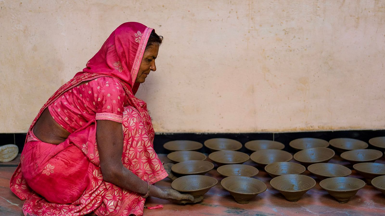 image of a woman draped in a pink saree lining up clay bowls on the floor