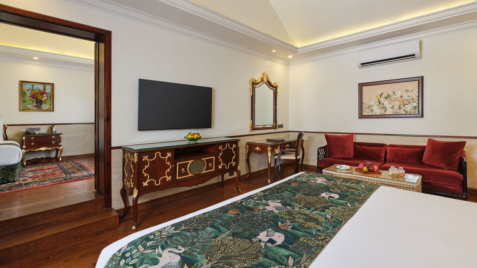 A bedroom with a comfortable bed, TV, sofa, cupboard and a door leading to another room at Mayfair Spa Resort and Casino.