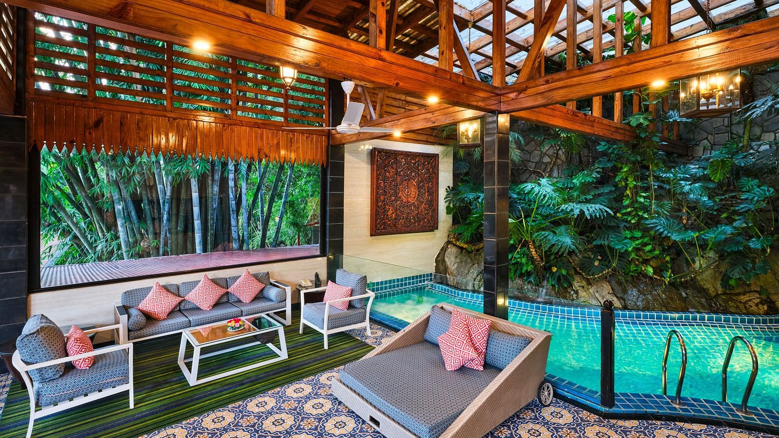 An artistic luxurious outdoor space of Grand Villa featuring a pool, patterned tile floor, outdoor seating, wooden structures, an lush greenery.