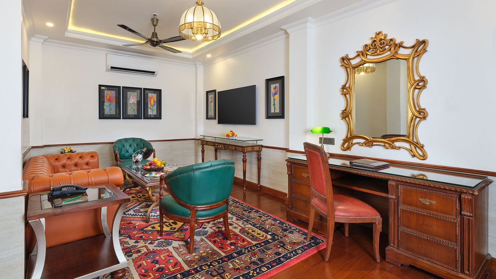 A seating area in Royal Villa with sofas, chairs and a table on a decorative rug, a wooden cabinet , TV and a mirror.