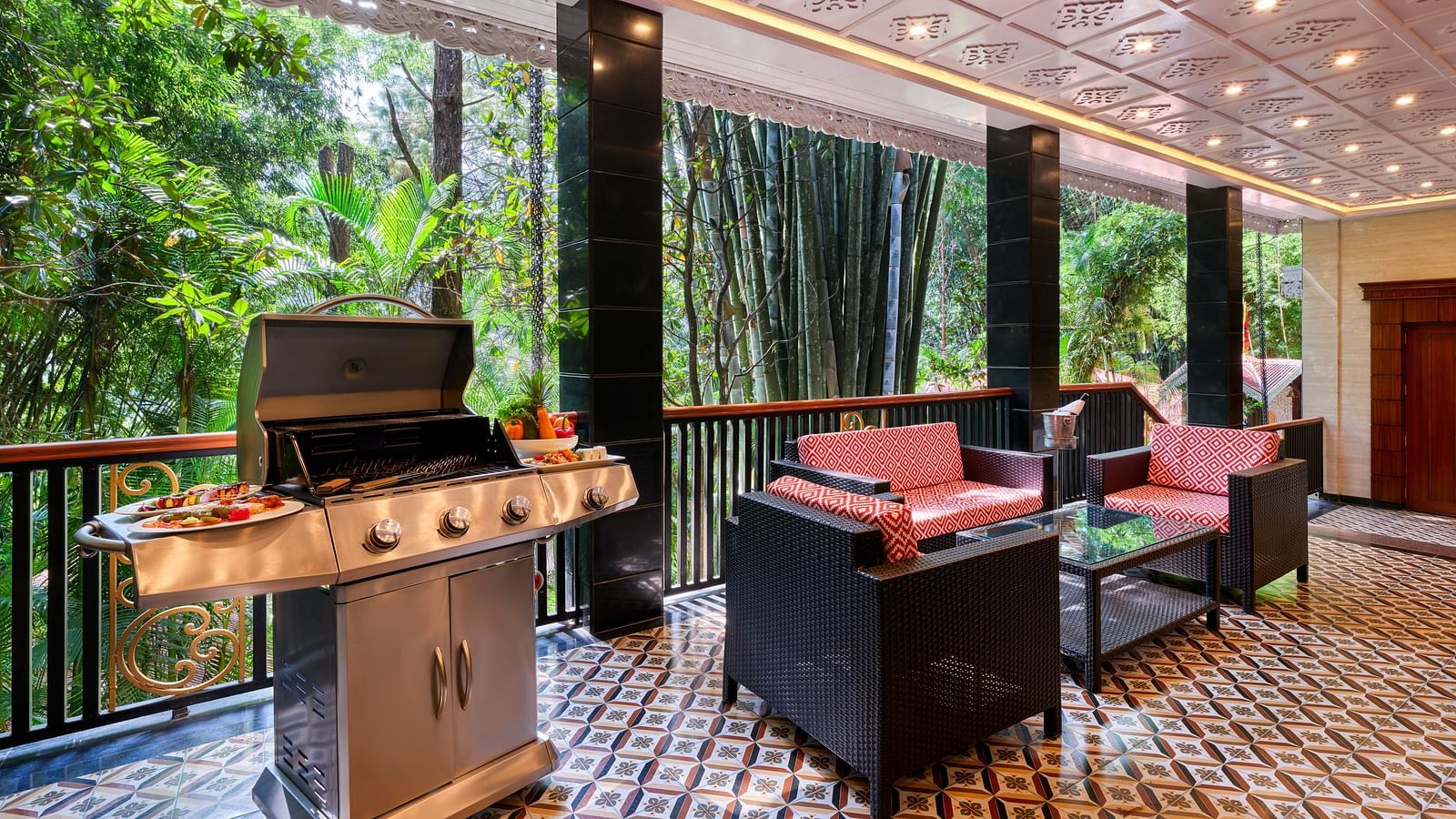 Royal Villa outdoor seating area with a barbecue grill , table, sofas and a balcony overlooking greenery.