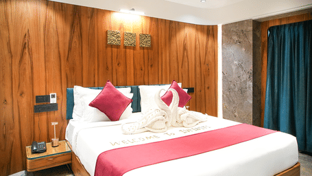 Wooden-panelled bedroom with king bed, red cushions, and dark curtains at Infiniti Hotel, Indore.