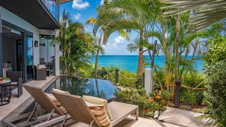 An oasis residences with sun loungers, pool, lush greenery, and ocean views under a bright sky at Tamarind Hills Resort and Villas - Antigua.