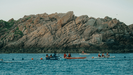 A group of people kayaking along a shoreline with a backdrop of mountain under a clear sky
