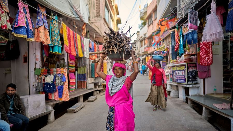 image of a woman wearing a pink half saree carrying firewood over her head through the streets in rajasthan