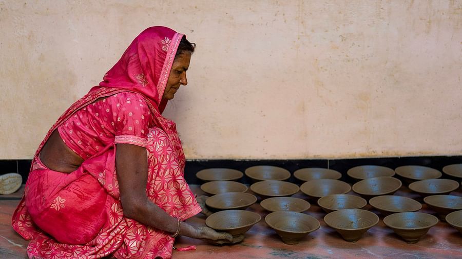 image of a woman draped in a pink saree lining up clay bowls on the floor