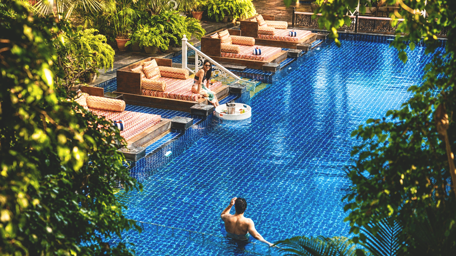 High-angle view of guests enjoying a resort swimming pool surrounded by tropical trees at MAYFAIR Palm Beach Resort, Gopalpur-on-Sea.