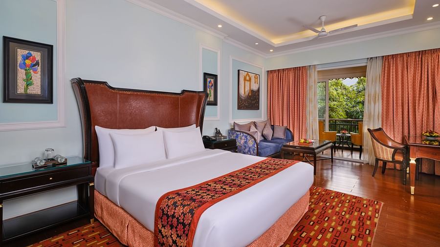 elegant Executive Room with a large bed, rug, tables, chairs, paintings on walls and large window with curtains overlooking greenery