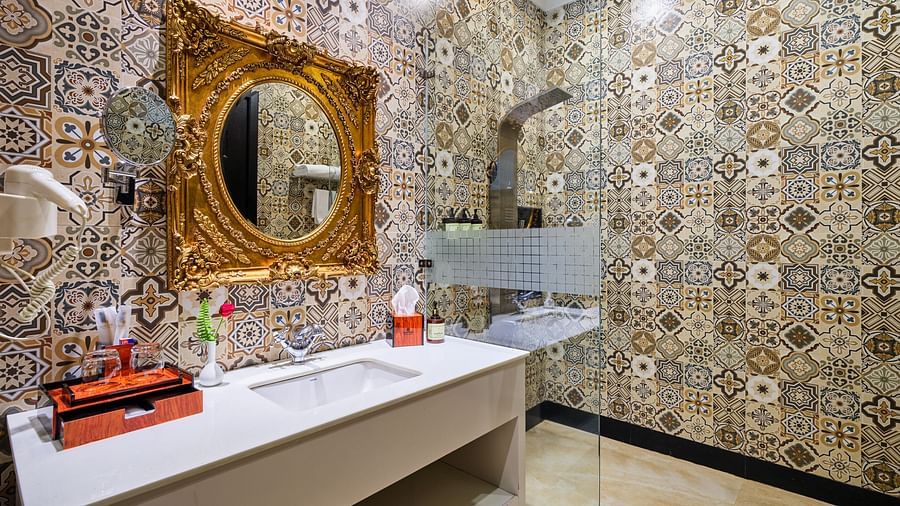 Executive Room Bathroom with tile flooring and matching ceiling. A large gold framed mirror hangs above a white cabinet with a sink. A glass separating  the walk in shower