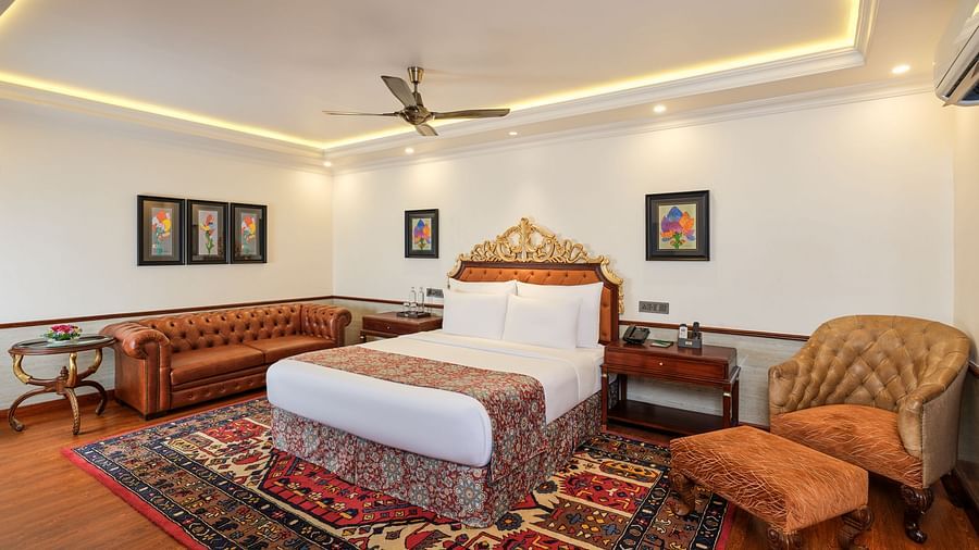 a luxurious Executive Suite with a large bed on a decorative rug, sofas, tables, artworks on white walls