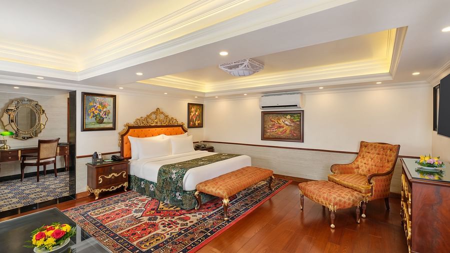 elegant Oriental Villa bedroom with a decorative rug beneath a grand bed, chair, table, TV and artworks on wall 