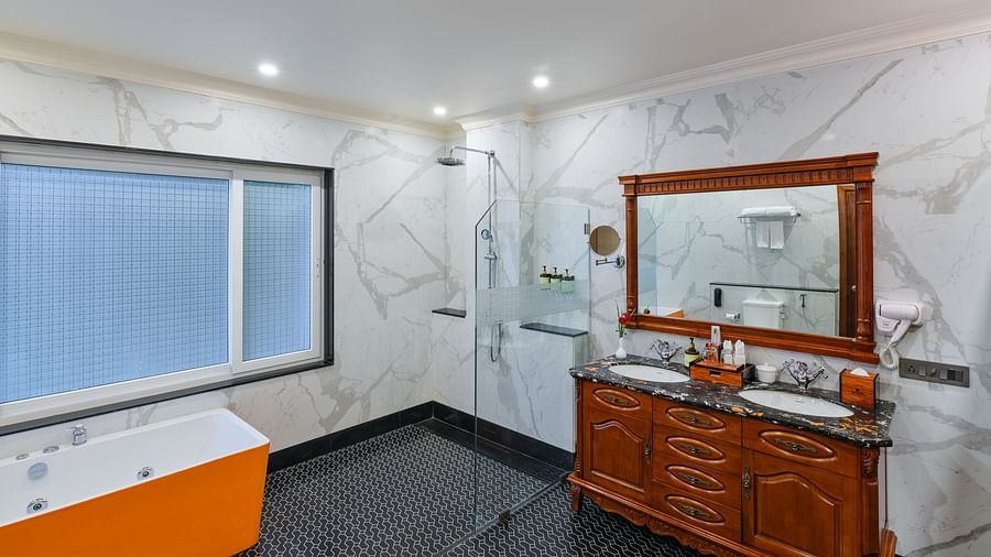 Oriental Villa  Bathroom with an orange bathtub, a black and white tiled floor, a large mirror with a wooden frame above two sinks, and a glass shower screen